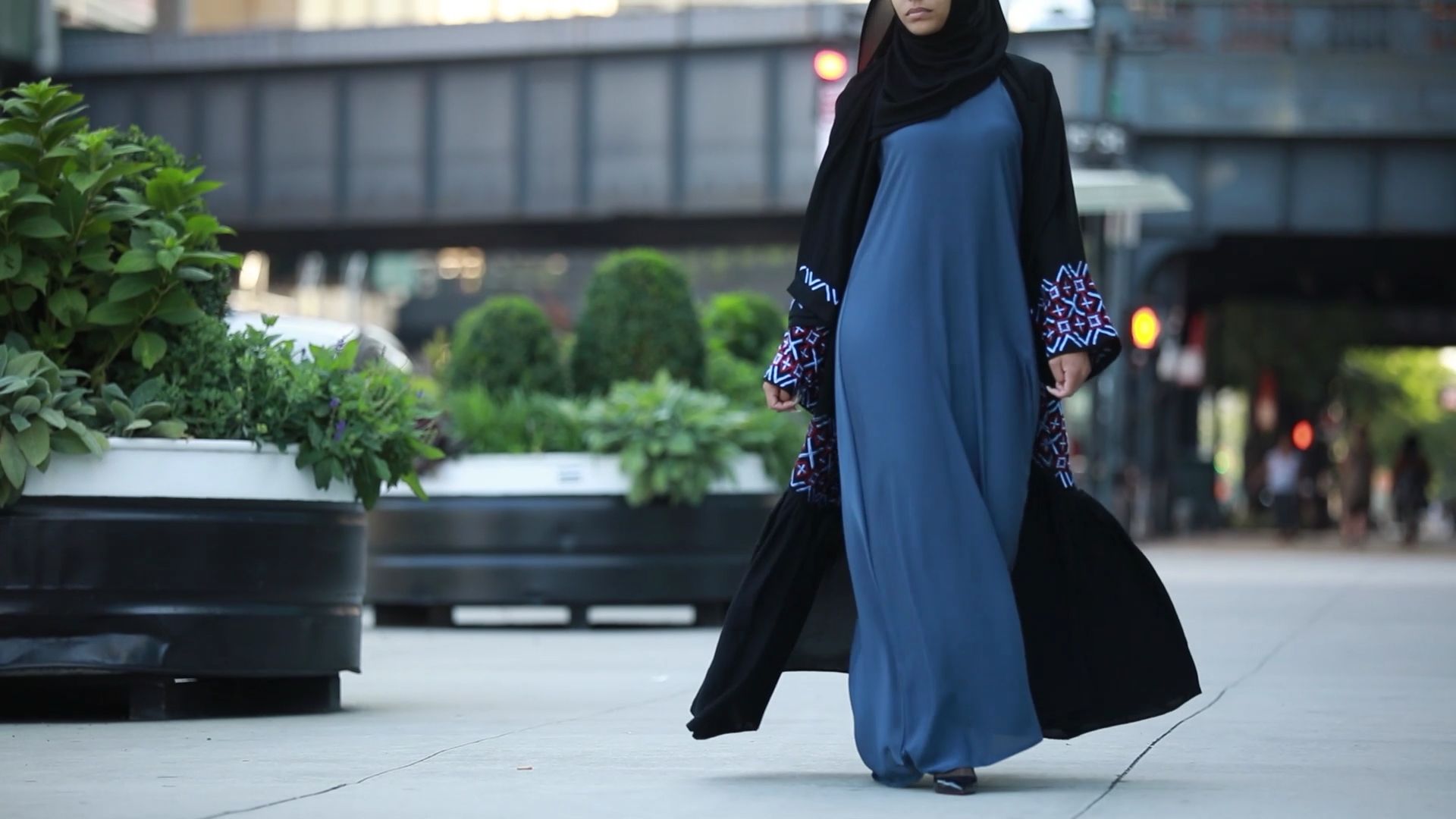 Woman in a blue abaya with black hijab walking on a city street.